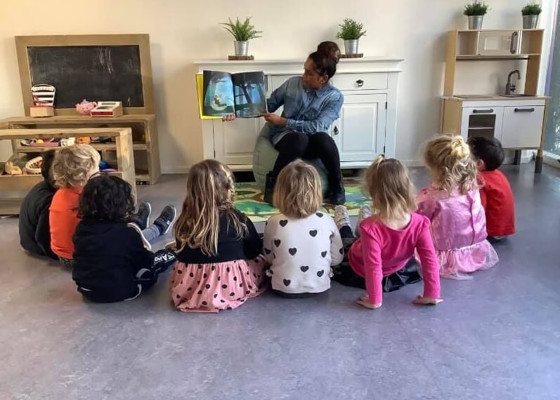 Pedagogisch medewerker leest voor aan de kinderen op de dagopvang