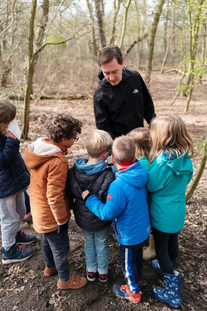 Pedagogisch medewerker geeft natuurles in het bos aan de bso-kinderen