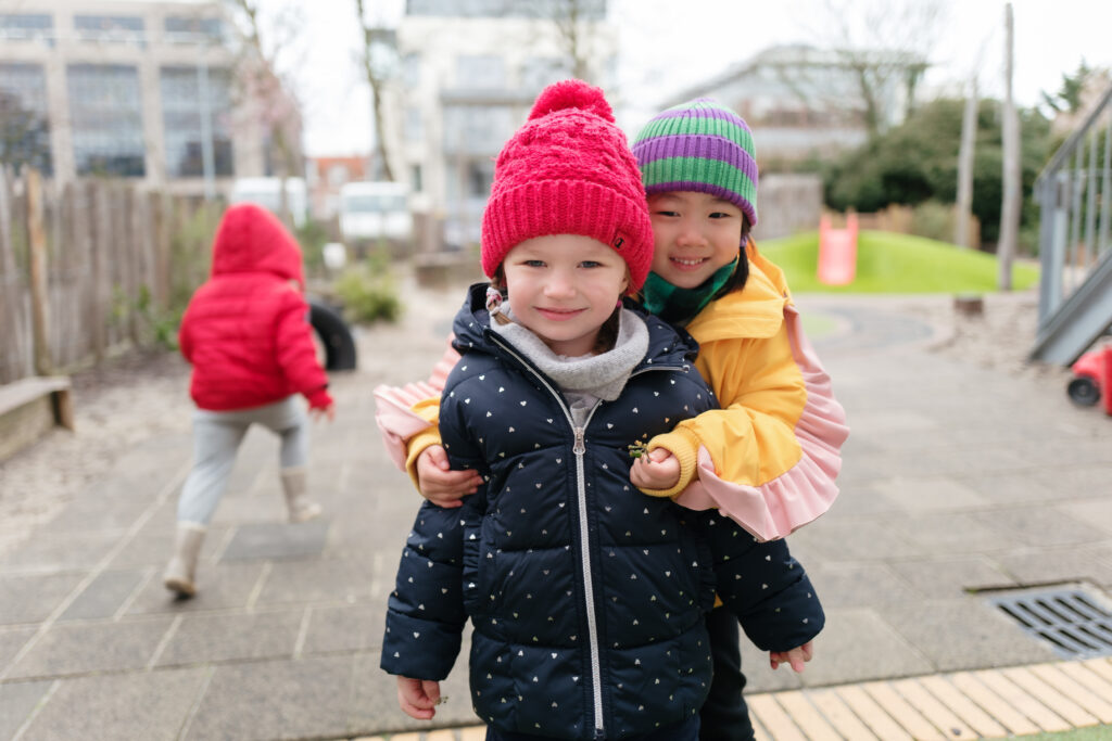 Twee meisjes poseren knuffelend voor de foto op het buitenplein van de internationale kinderopvang