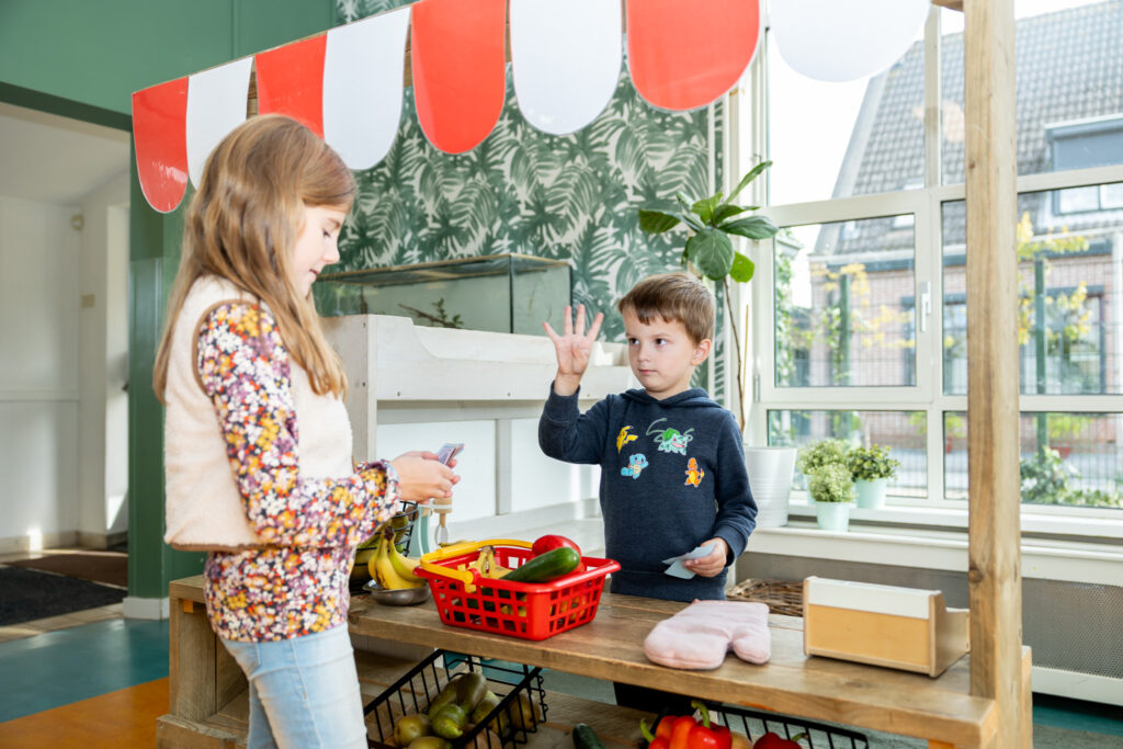 Twee kinderen spelen klant en verkoper op de kinderopvang. Het jongetje zegt het meisje hoeveel iets kost.