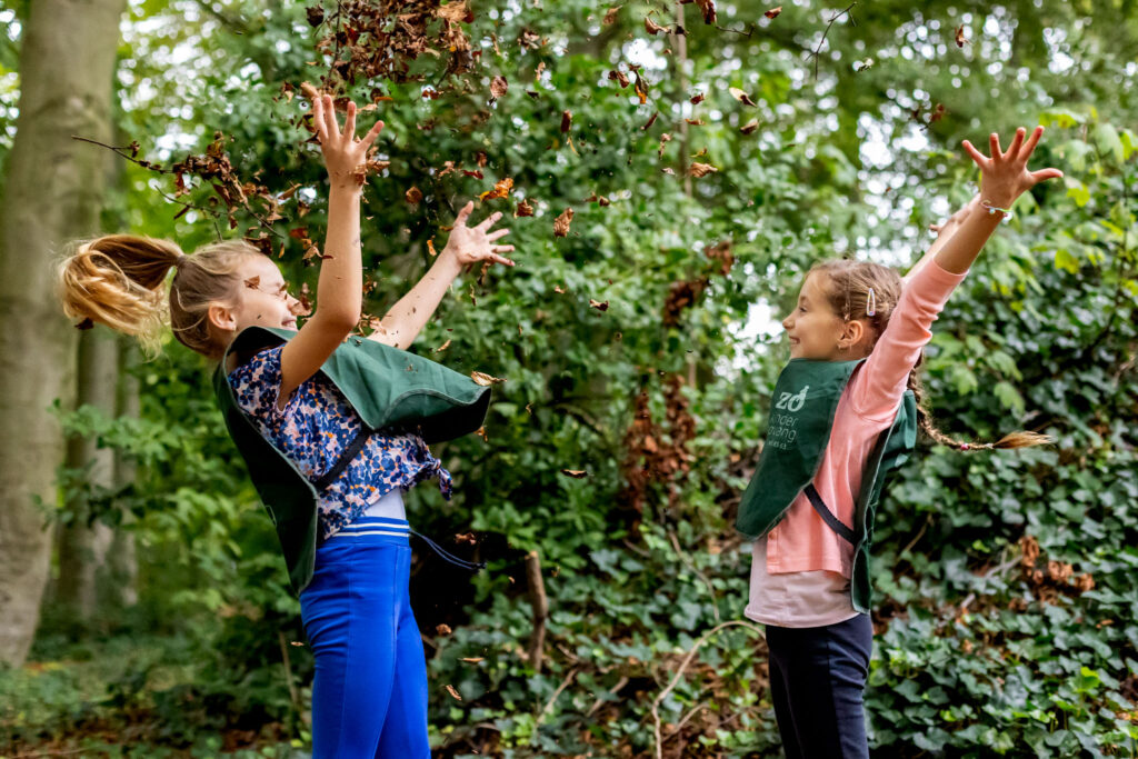 Two girls playing in the woods and throwing leafs in the air