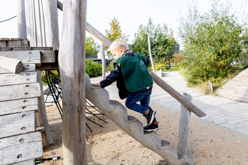 Jongetje klimt op trap in het buiten-klimhuisje op de kinderopvang