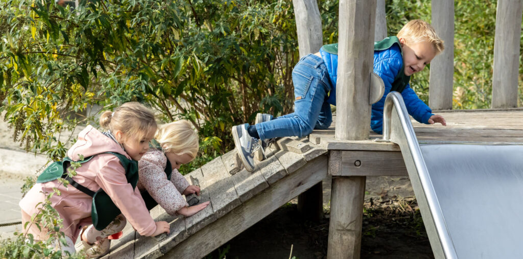 Kinderen klimmen en klauteren in de buitenspeeltuin op de kinderopvang