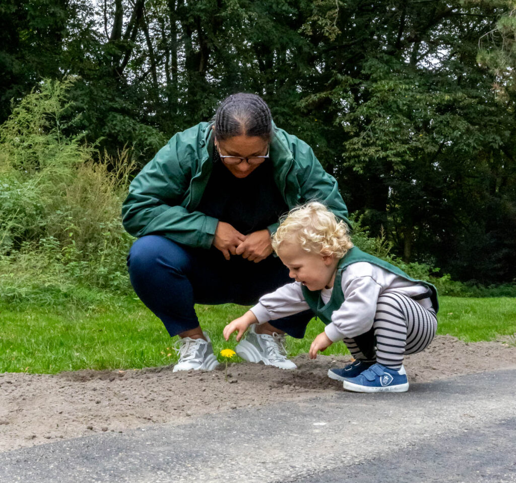 Pedagogisch medewerker kijkt met een spelend kind naar een paardenbloem