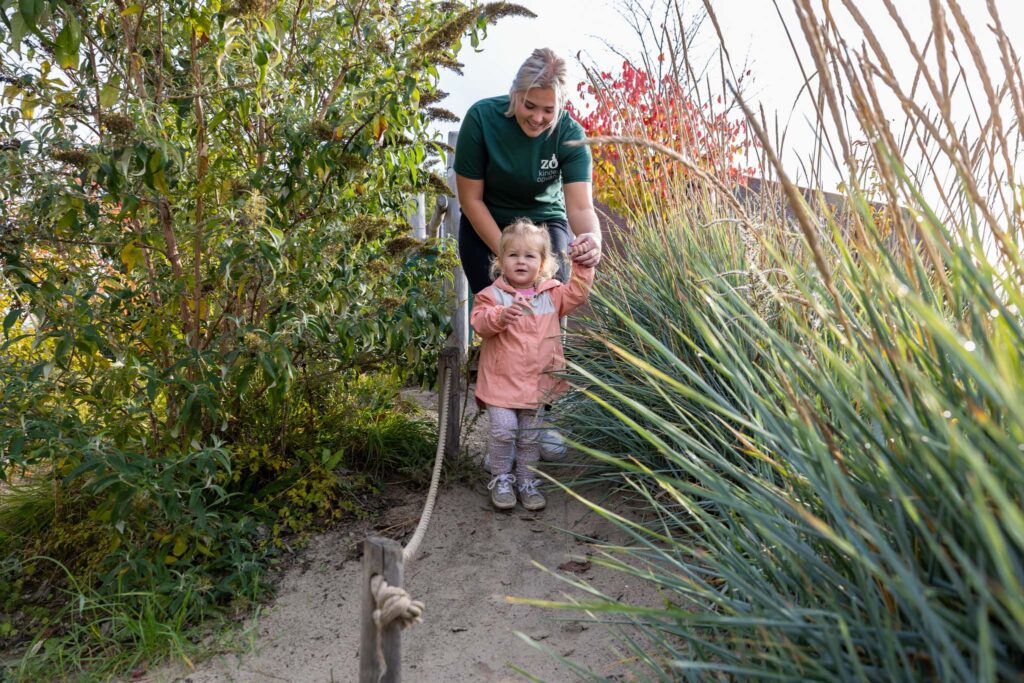 Pedagogisch medewerker helpt een kind op de zandheuvel tijdens het buitenspelen