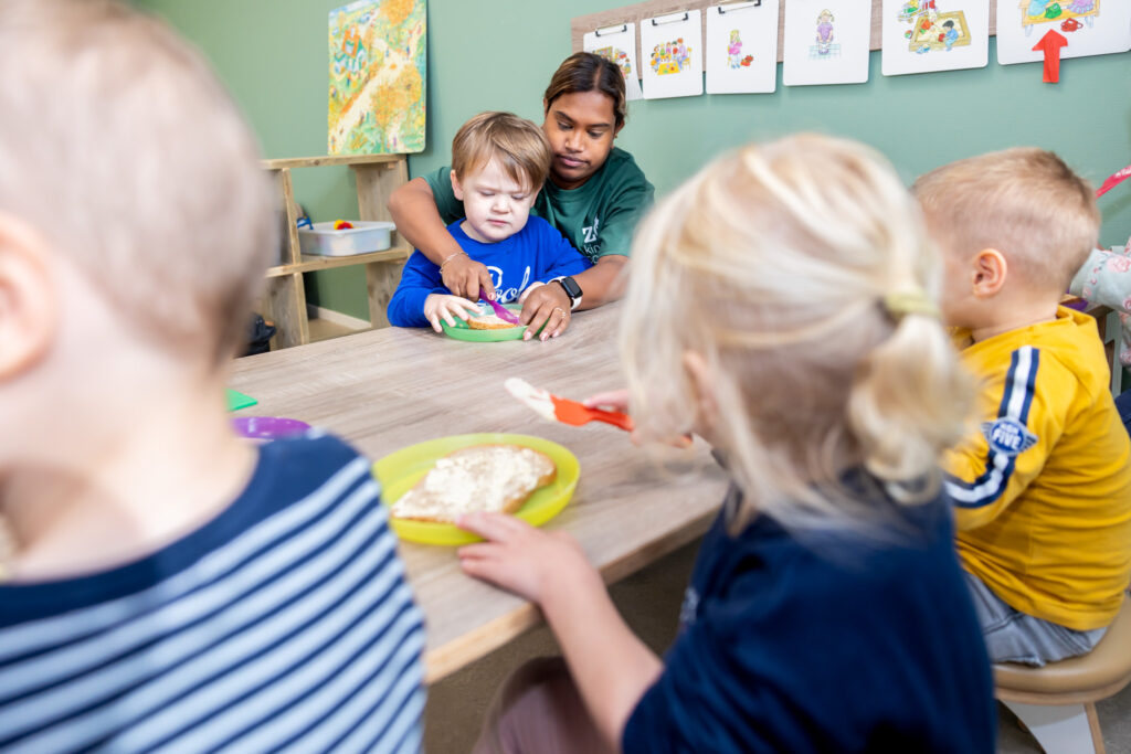 Pedagogisch medewerker helpt een kind om een boterham te snijden op de dagopvang